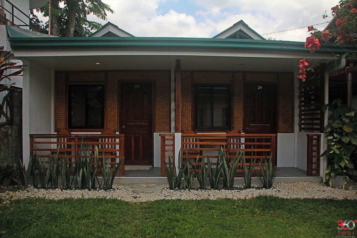 A two-story house with a green roof, two doors, and a porch with wooden benches.