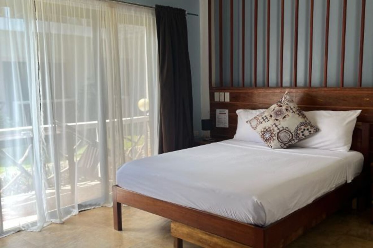 Una cama bien hecha con un cojín estampado, un cabecero de madera y cortinas de gasa.