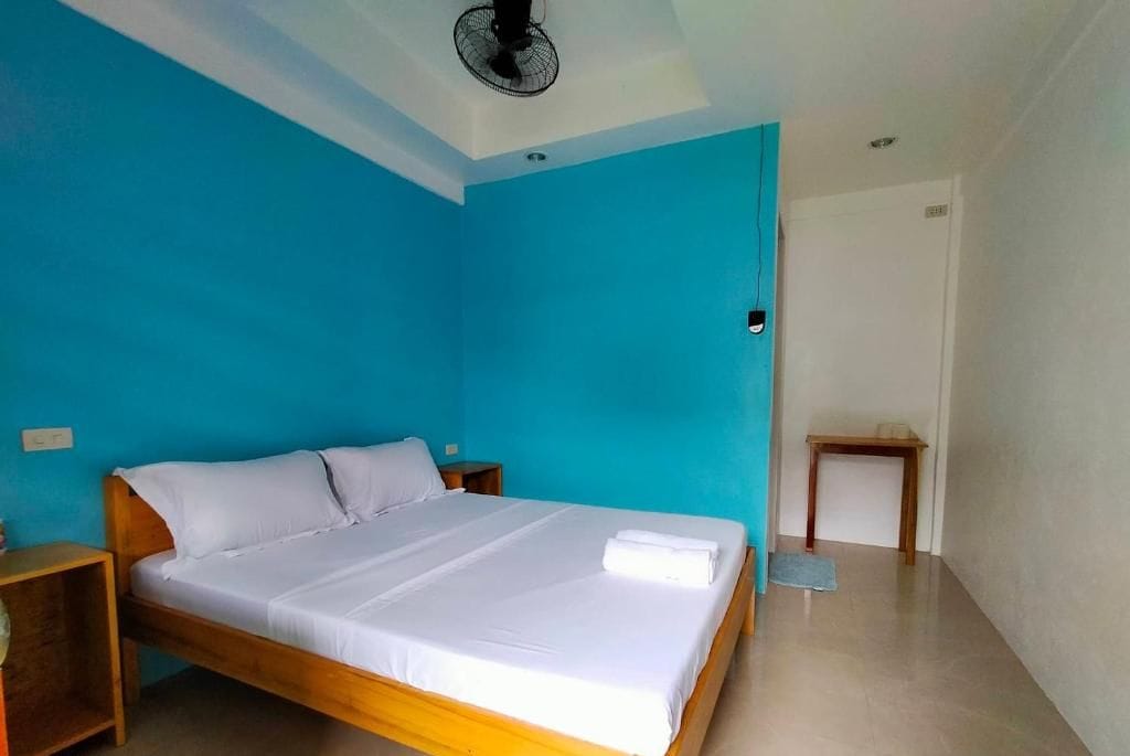 A room with a bed, a nightstand, a wooden table, and a ceiling fan.