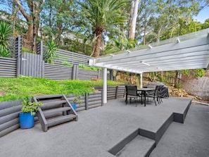 A covered outdoor patio with a pergola, seating area, and a stone wall.