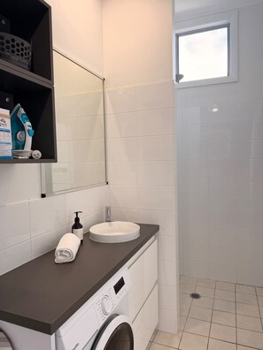 A modern bathroom with a built-in washing machine, a sink, and a shower area.