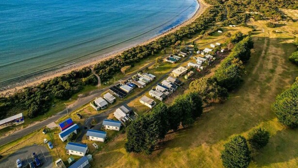 Una zona costera con una hilera de casas móviles a lo largo de la playa, una carretera que lleva a la playa y una masa de agua al fondo.