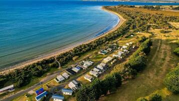 A coastal area with a row of mobile homes along the beach, a road leading to the beach, and a body of water in the background.