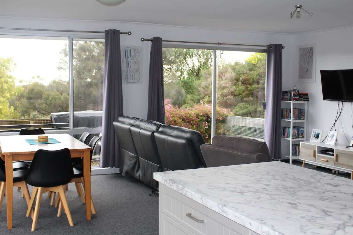 A room with a dining table, chairs, a sofa, a TV, and a large window with curtains.
