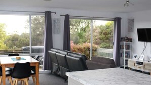 Una habitación con una mesa de comedor, sillas, un sofá, un televisor y un amplio ventanal con cortinas.