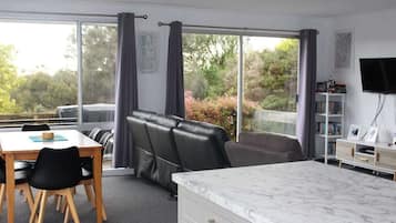 A room with a dining table, chairs, a sofa, a TV, and a large window with curtains.
