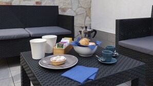 A dining area with wicker furniture, a stone wall, and a table set with a plate of food, cups, and a napkin. - 4 Bedrooms Apt in Sorrento Center | location&view (Sorrento)