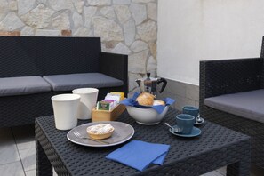 A dining area with wicker furniture, a stone wall, and a table set with a plate of food, cups, and a napkin.
