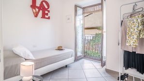 A small, modern bedroom with a single bed, a bedside table with a lamp, a red 'LOVE' sign on the wall, and a balcony with a view of greenery. - 4 Bedrooms Apt in Sorrento Center | location&view (Sorrento)