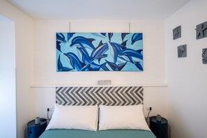 Een slaapkamer met een bed, twee nachtkastjes, een kunstwerk van dolfijnen aan de muur, en een 'RELAX' bord boven het bed.