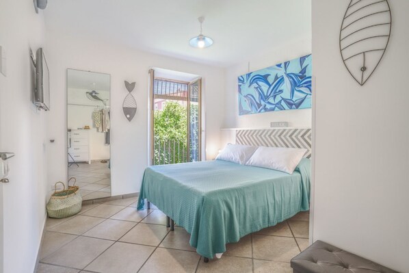 A bedroom with a bed, a window, a door, and a wall-mounted artwork.