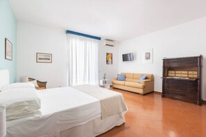 A bedroom with a bed, a sofa, a dresser, and a television on the wall.