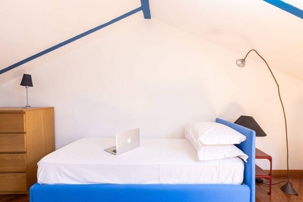 A bedroom with a bed, a laptop, a lamp, and a dresser.