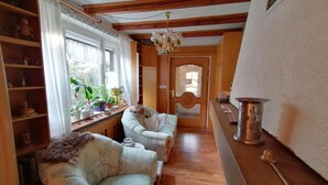 A cozy living room with a sofa, a wooden coffee table, and a chandelier. There are potted plants on a shelf and a door leading to another room. - Apartment 'Haus Am Waldrand' with Mountain View, Private Terrace and Wi-Fi (Freital)
