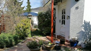 A house with a stone pathway leading to the entrance, surrounded by various potted plants and a solar panel on the roof. - Apartment 'Haus Am Waldrand' with Mountain View, Private Terrace and Wi-Fi (Freital)