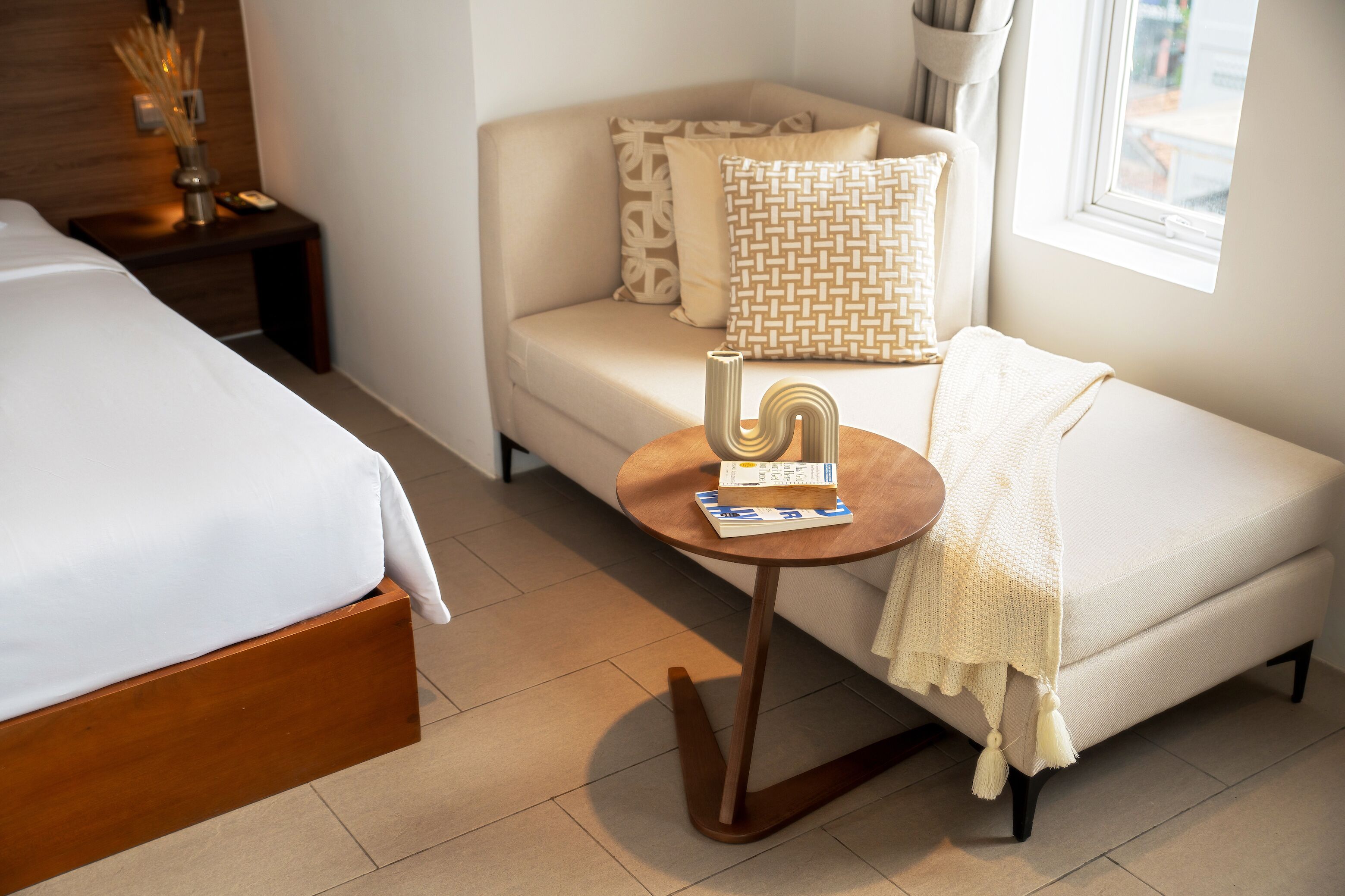 A hotel room with a bed, a sofa, a small round table with a book, and a window.