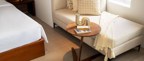 A hotel room with a bed, a sofa, a small round table with a book, and a window.