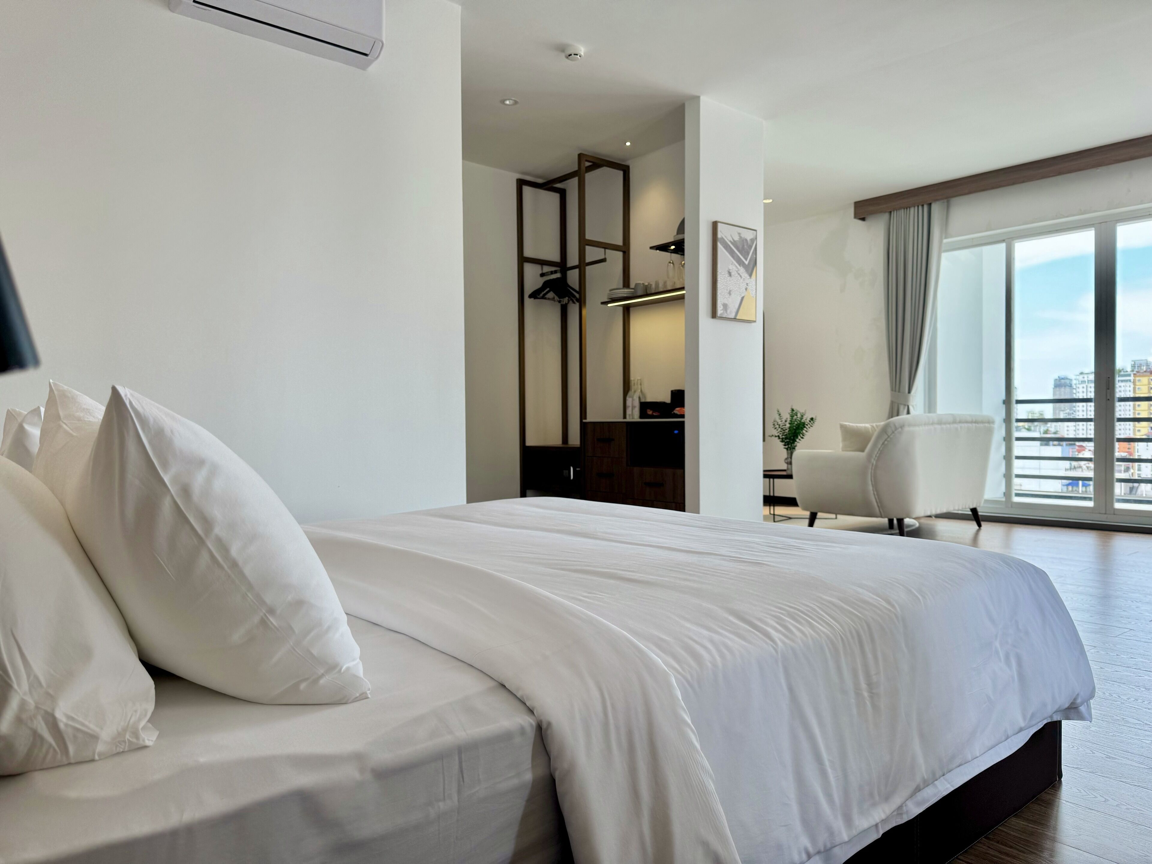 A hotel room with a large bed, a chair, a desk, and a view of the city through the window.