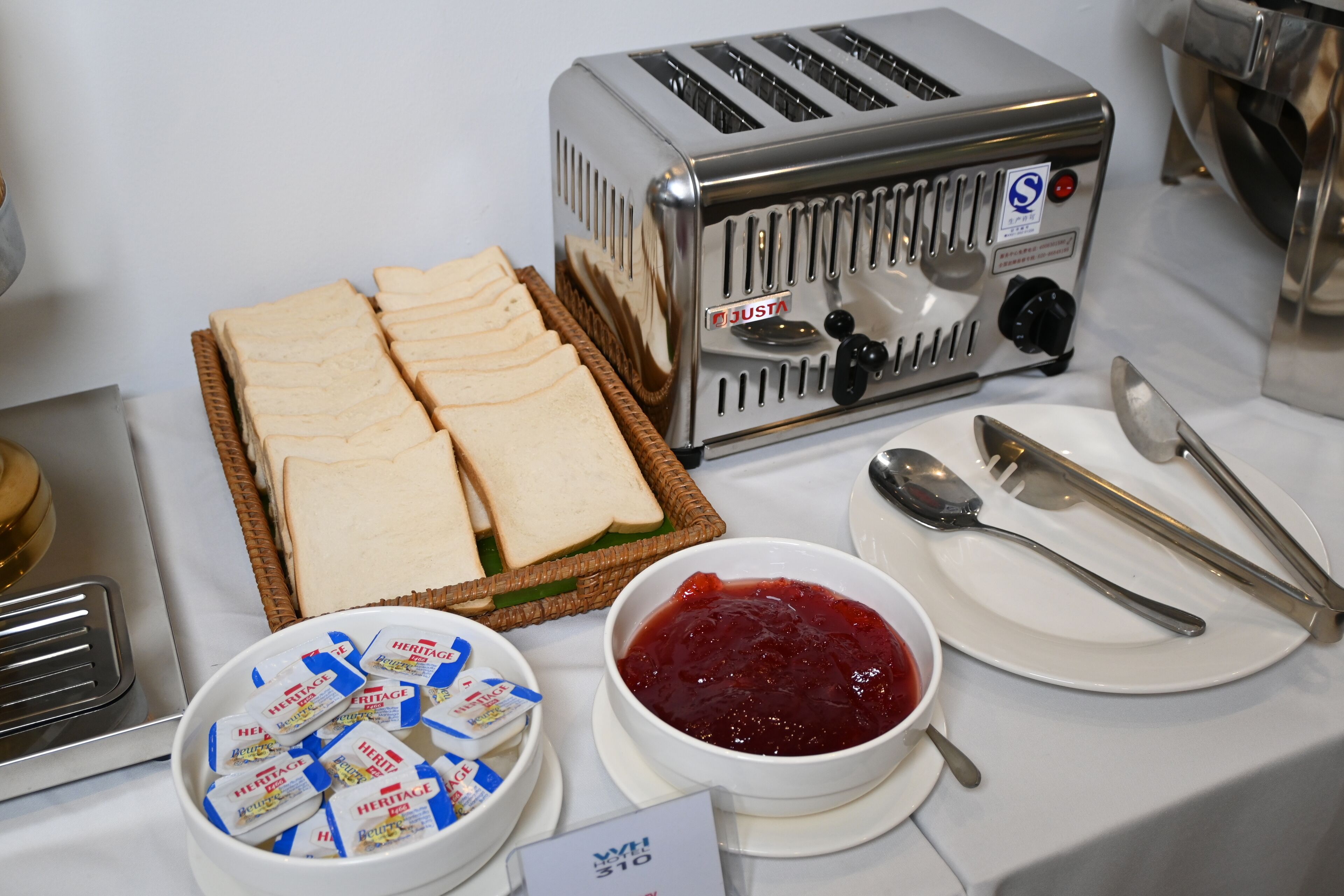 A breakfast setup with a toaster, sliced bread, jam, and condiments.