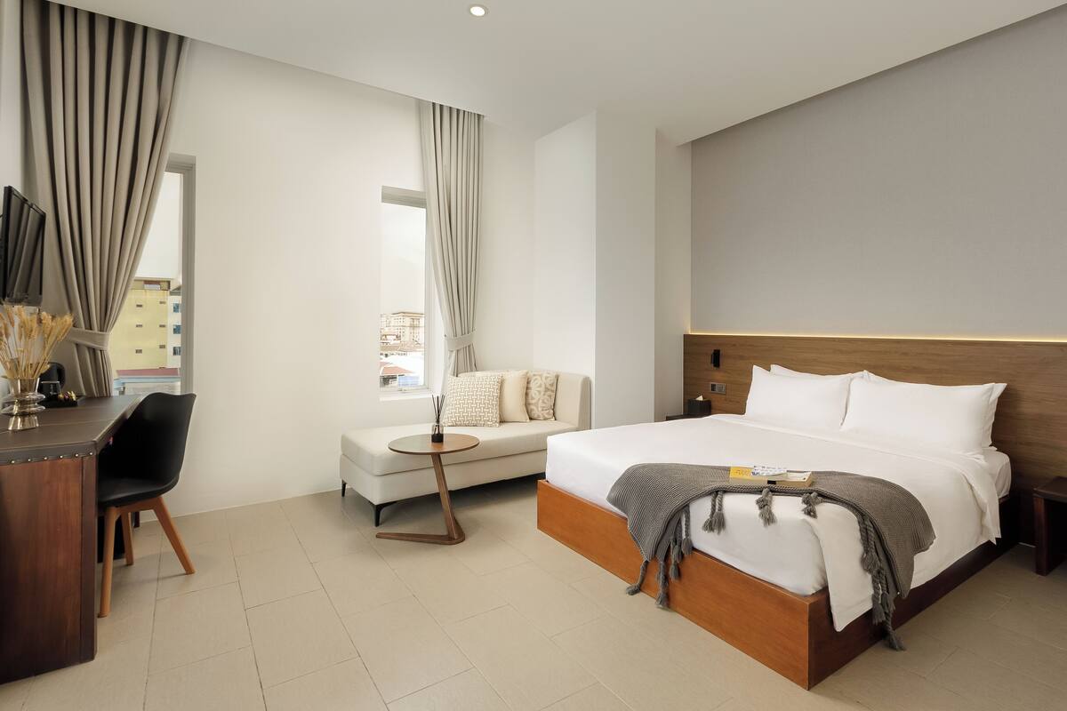 Una habitación de hotel moderna con una cama grande, un sofá, un escritorio y vistas a la ciudad.
