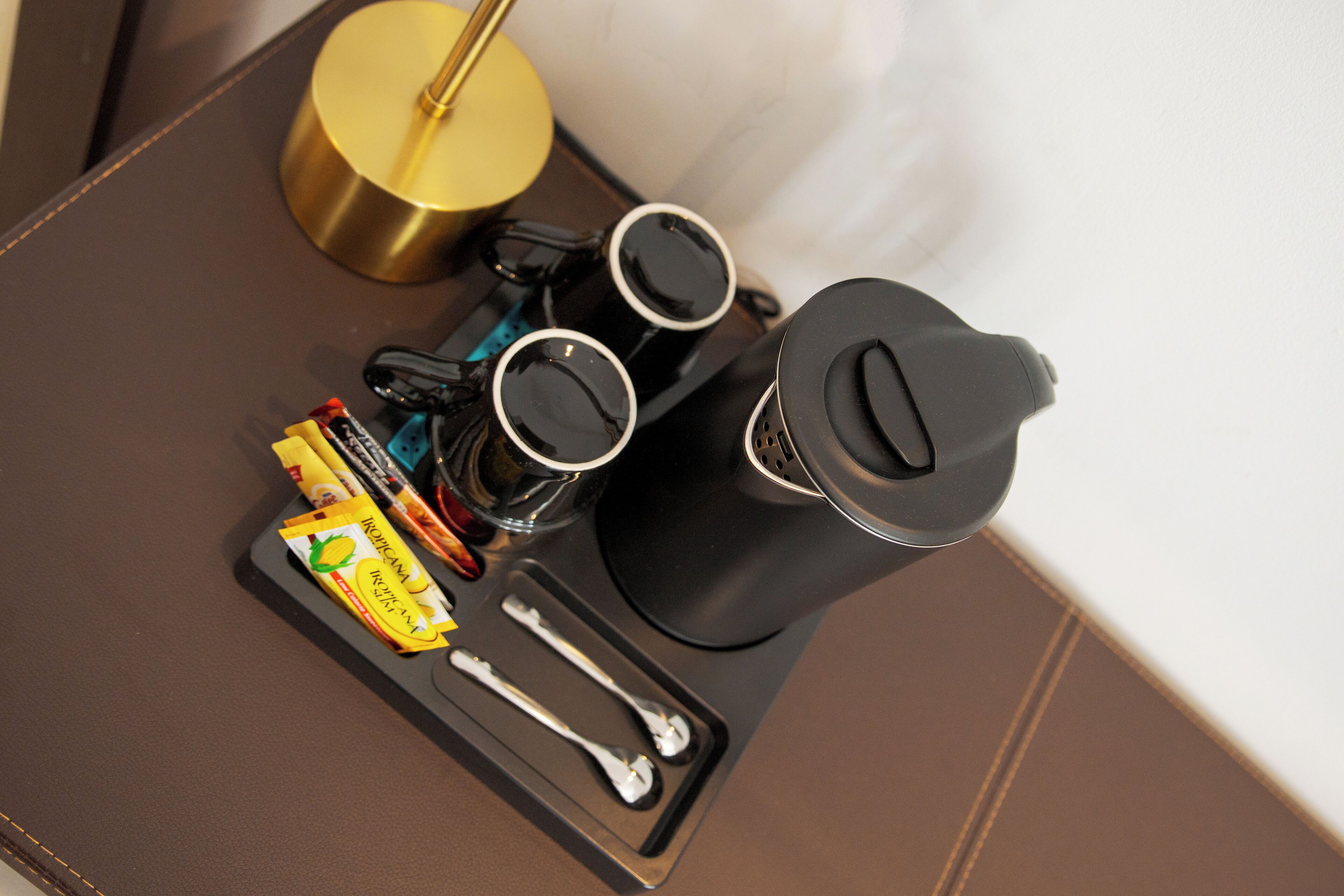 A coffee maker with two cups, a spoon, a packet of sugar, and a gold-colored object on a tray.