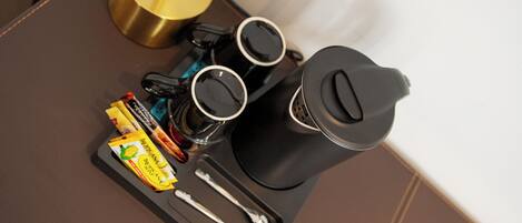 A coffee maker with two cups, a spoon, a packet of sugar, and a gold-colored object on a tray.
