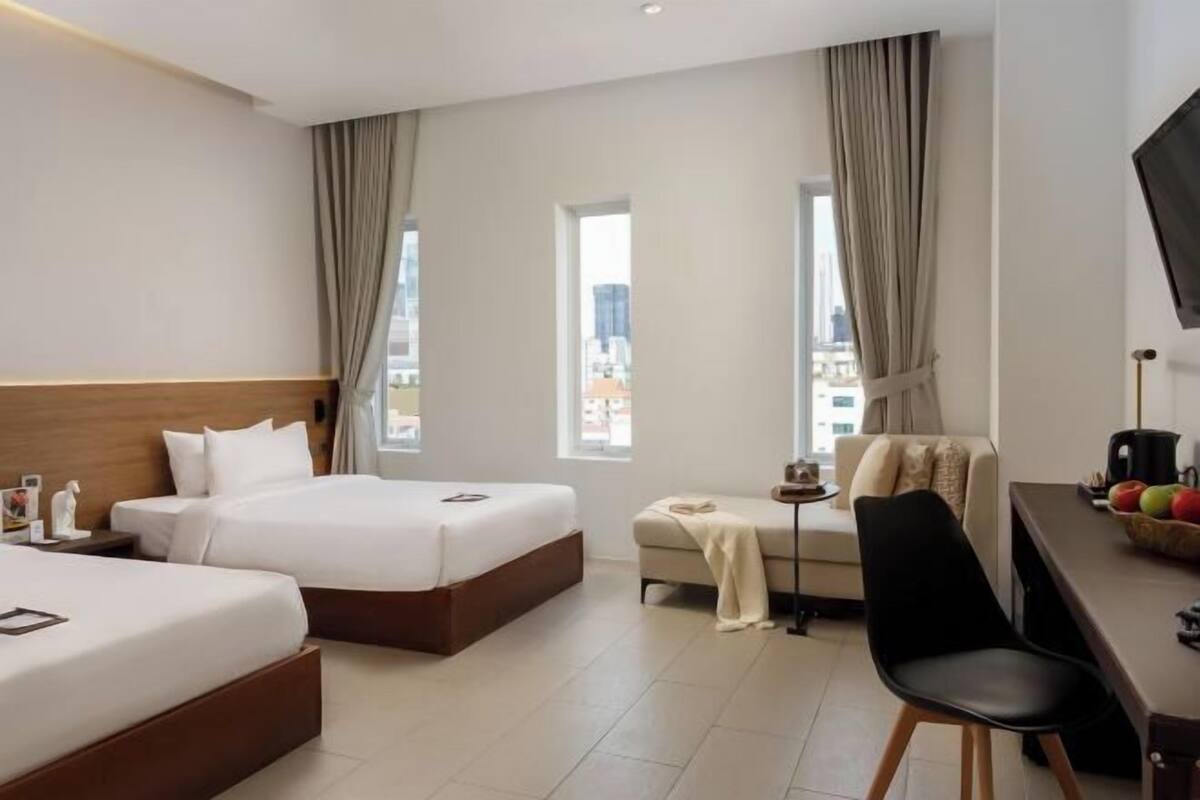Habitación de hotel con dos camas, un sofá, un escritorio con silla y un televisor.