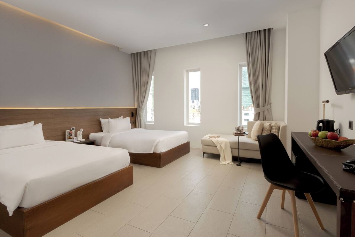Habitación de hotel con dos camas, un escritorio, una silla, un televisor y una ventana con cortinas.