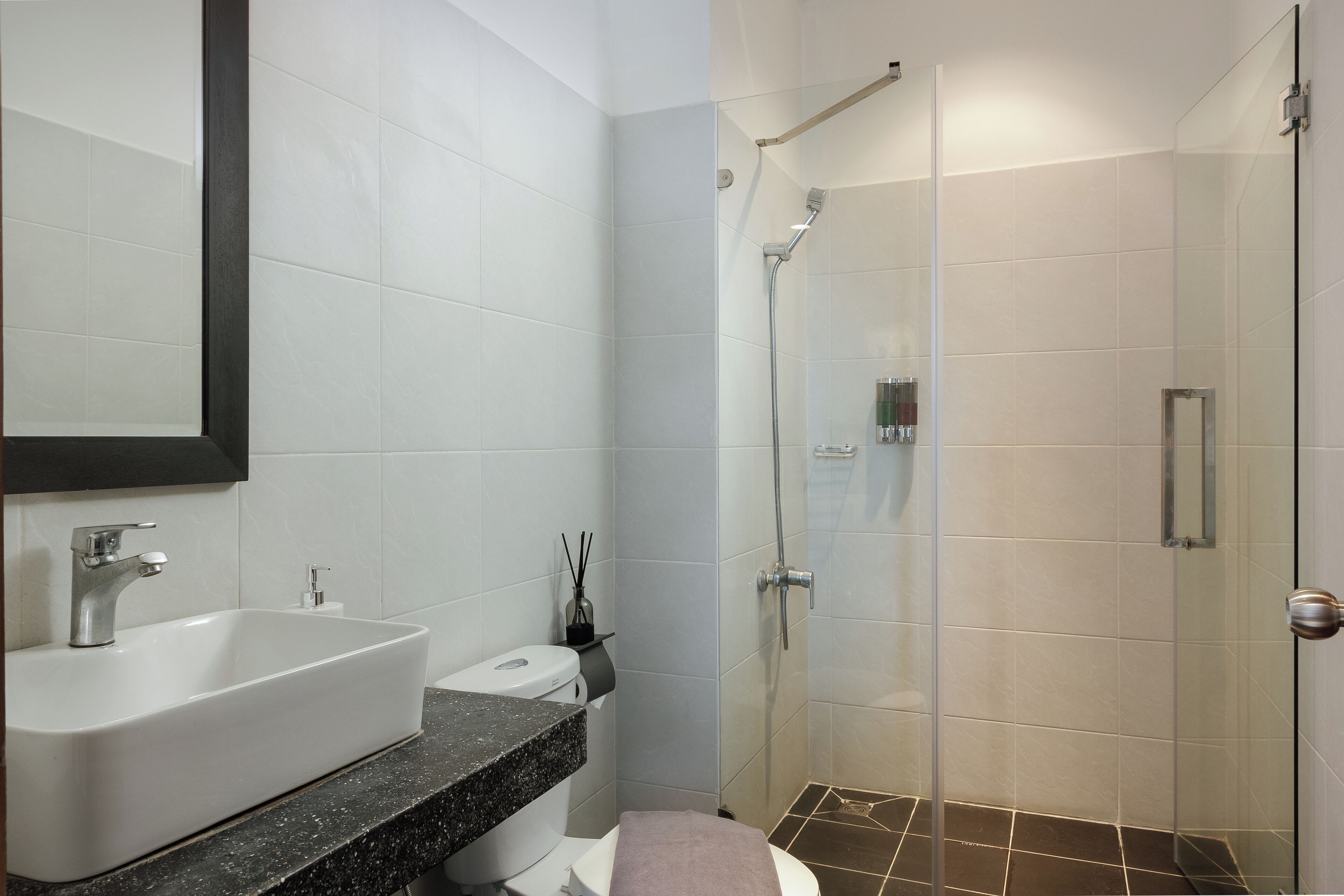 Un baño moderno con un lavamanos grande y blanco, un inodoro y una zona de ducha con mampara de vidrio.