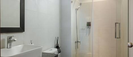 Un baño moderno con un lavamanos grande y blanco, un inodoro y una zona de ducha con mampara de vidrio.