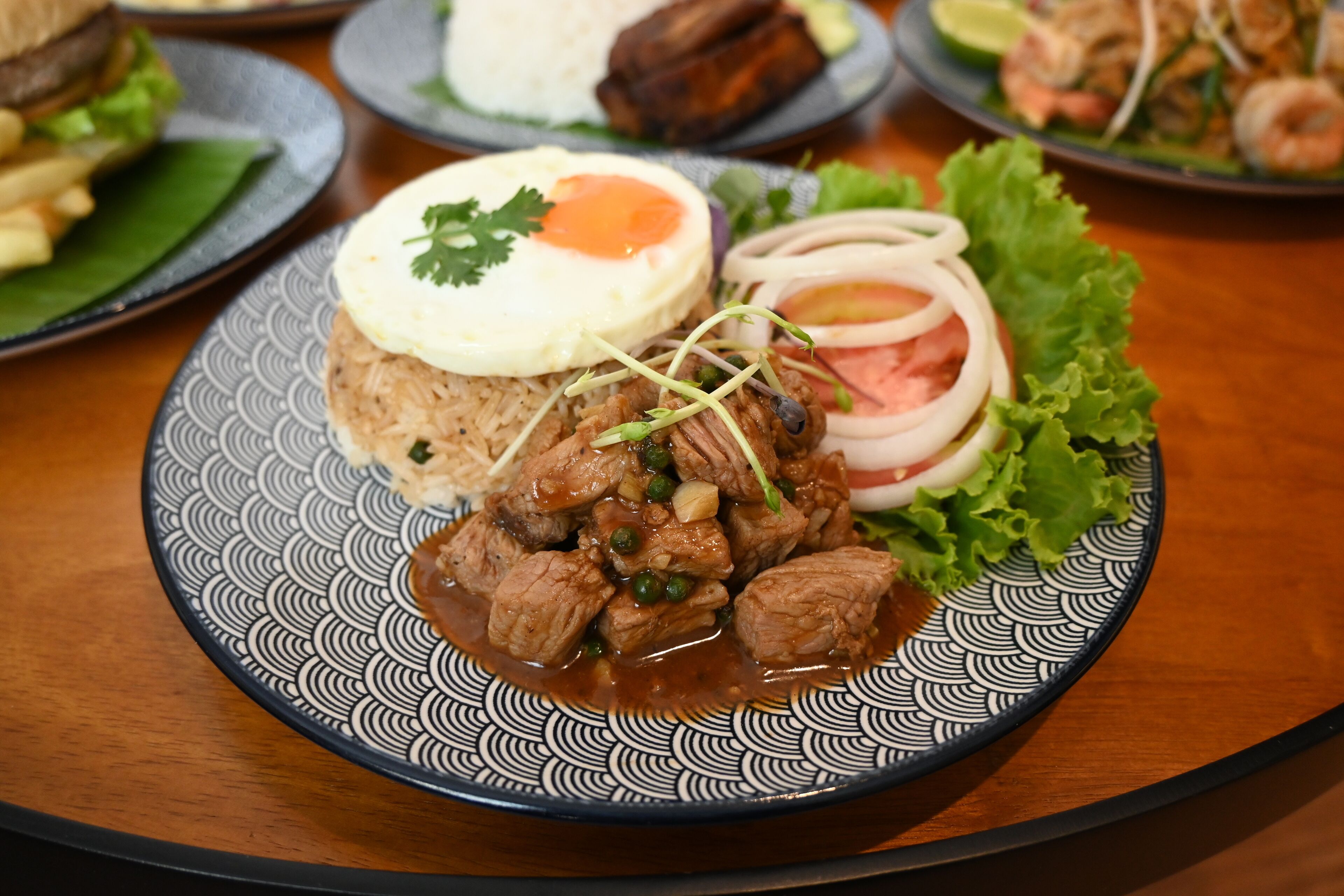 A plate of food with rice, meat, and a fried egg on a patterned plate.