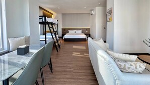 A modern hotel room with a bed, a dining table with chairs, a sofa, and a small table with a lamp. - WH Hotel 310  (Phnom Penh)
