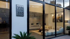 A modern hotel entrance with a glass facade, a reception desk, a sofa, and a coffee table. - WH Hotel 310  (Phnom Penh)