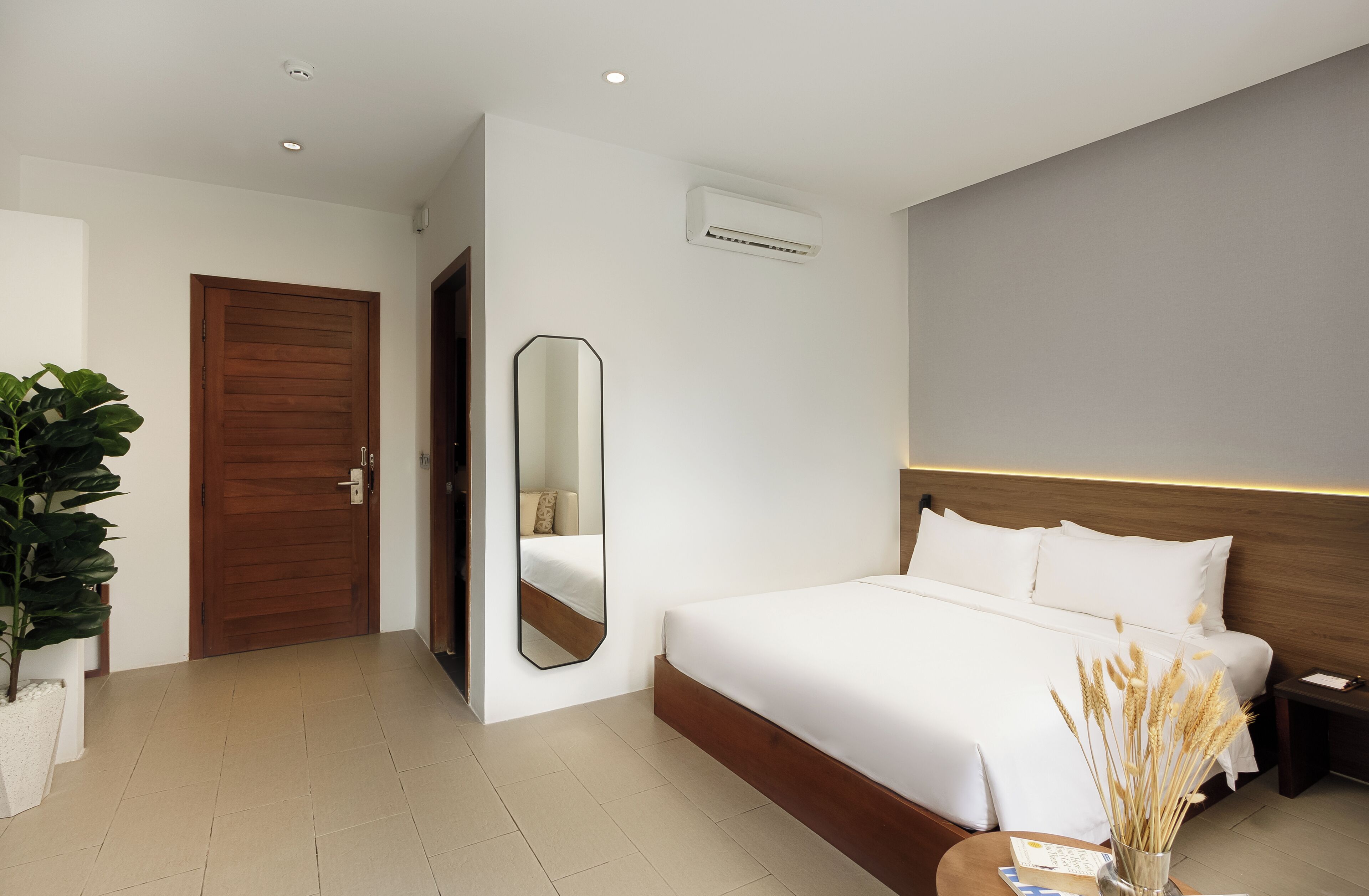 Una habitación de hotel moderna con una cama grande, una puerta de madera, un espejo y una planta en maceta.