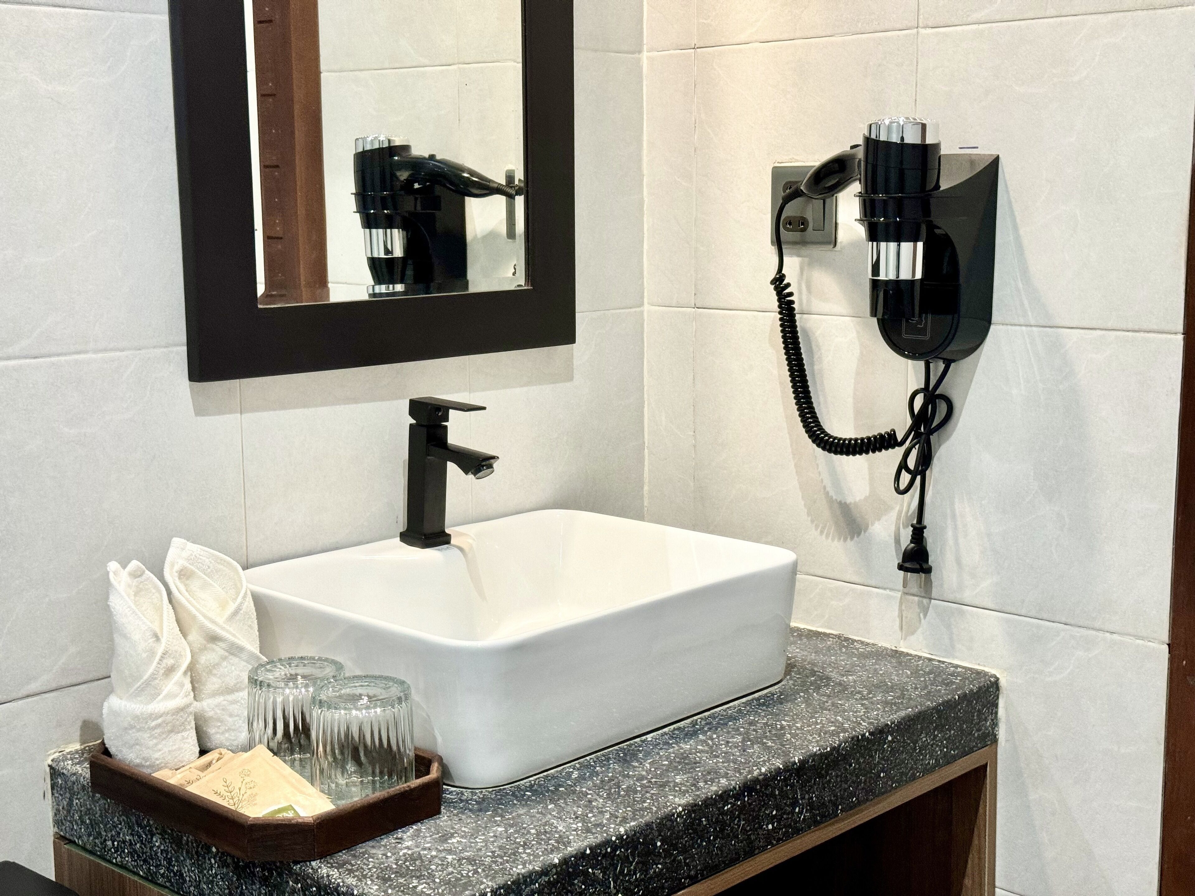 Un baño con un lavamanos blanco, grifo negro y un secador de pelo fijado en la pared.
