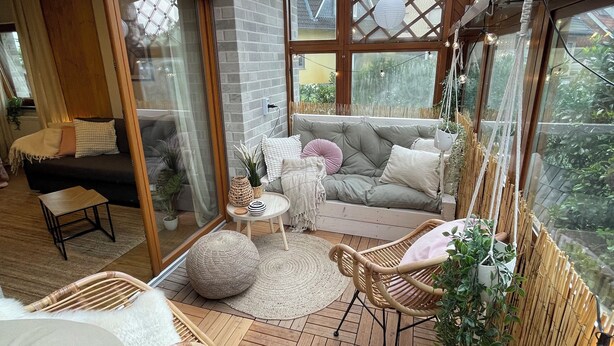A cozy, well-lit sunroom with a wooden floor, comfortable seating, and large windows offering a view of the outdoors. - Cozy apartment with conservatory near the safari park - dogs welcome (Verl)