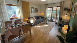 A cozy living room with a sofa, dining table, and chairs, a small coffee table, and a view of the outside through a sliding glass door. - Cozy apartment with conservatory near the safari park - dogs welcome (Verl)