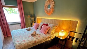 A bedroom with a bed, a nightstand, a lamp, a mirror, and a window with curtains. - Cozy apartment with conservatory near the safari park - dogs welcome (Verl)