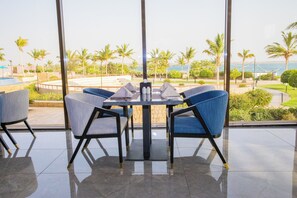 A dining area with a table and chairs, large windows with a view of palm trees and a body of water. - Royal Lazure Resort (Duba)