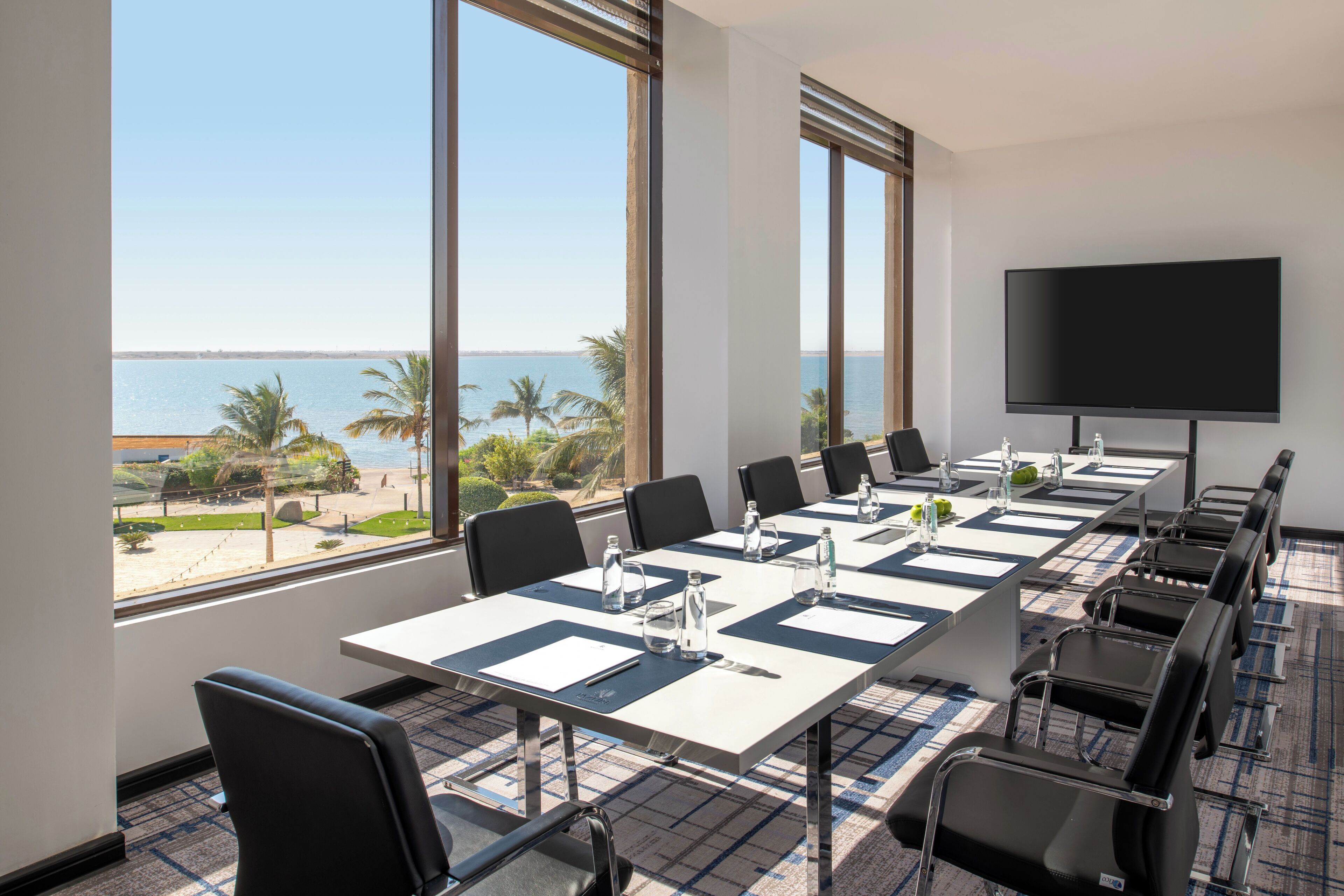Ein Konferenzraum mit großem Tisch, Stühlen, einem Flachbildfernseher und Blick aufs Meer.