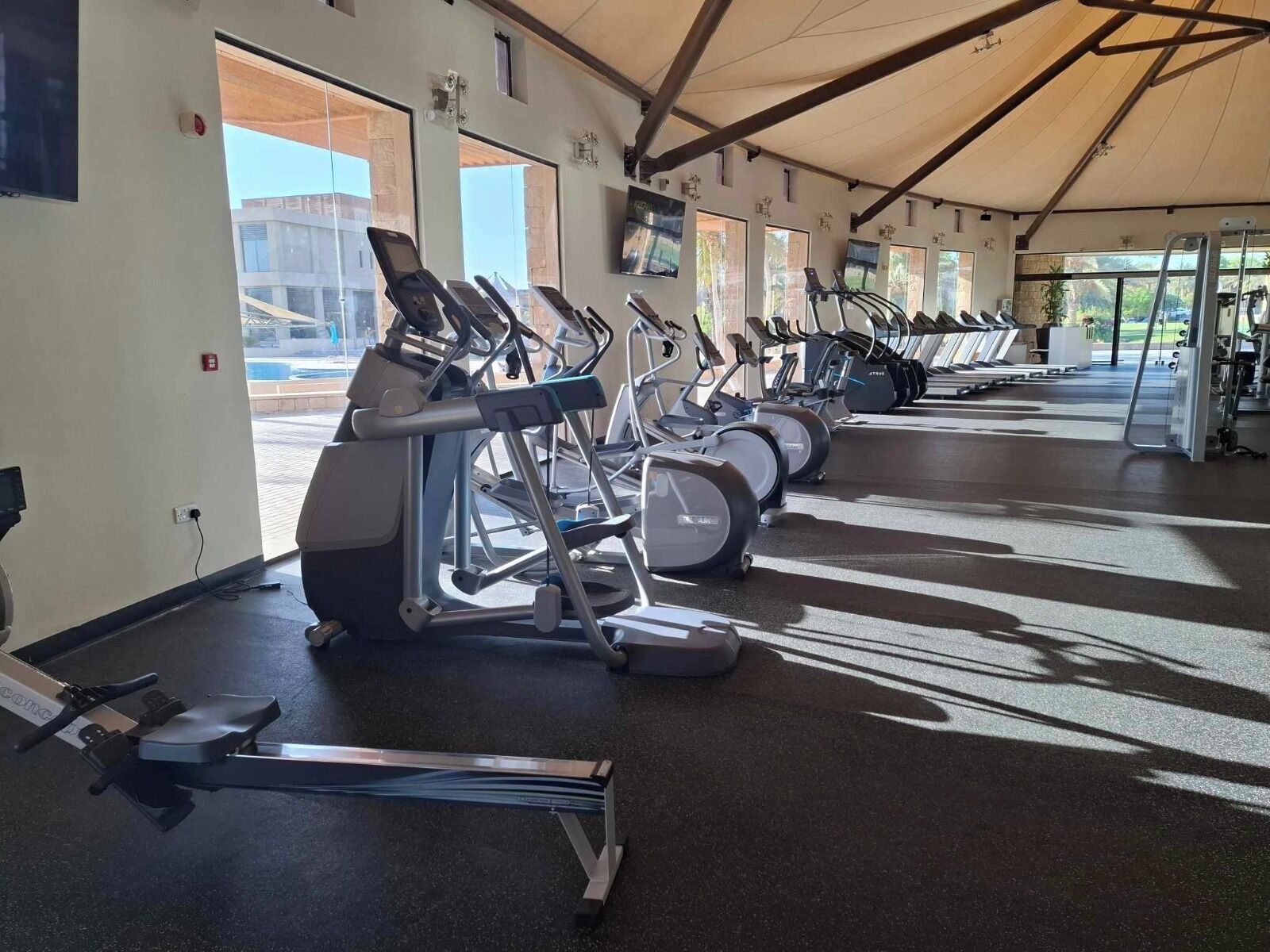 A gym with multiple treadmills and exercise equipment, large windows, and a ceiling with beams.