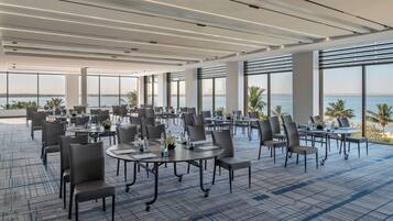 A spacious conference room with tables and chairs, large windows, and a view of the sea.