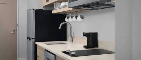 A modern kitchen with a built-in dishwasher, a black refrigerator, a microwave, and a coffee machine.