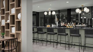 A modern bar area with a long counter, multiple stools, and a variety of bottles and glasses. - TownePlace Suites by Marriott Paris (Paris)