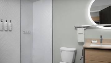 A modern bathroom with a herringbone tile wall, a shower, a toilet, a sink with a mirror, and toiletries on the wall.