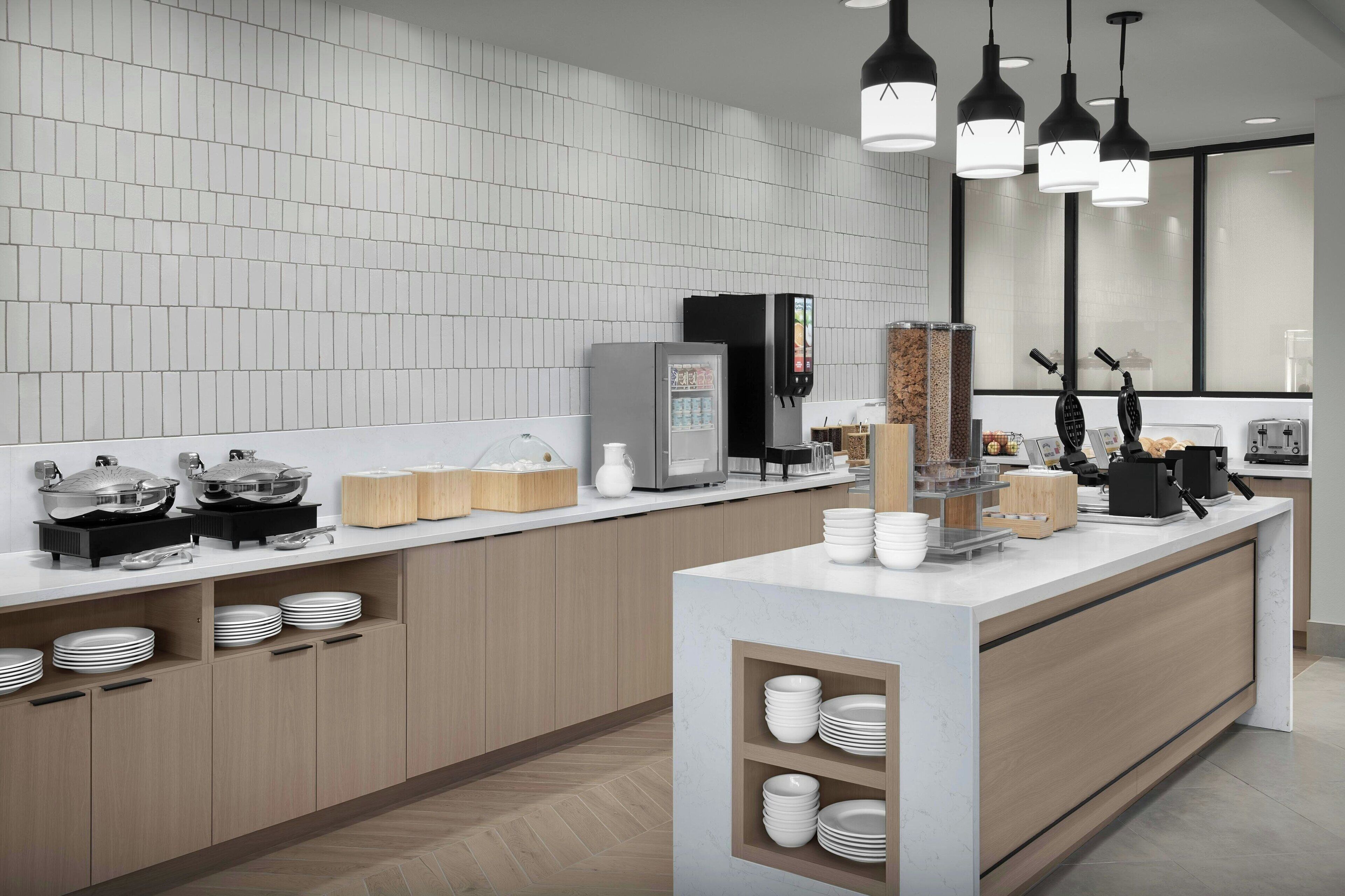 A modern kitchen with a white tiled backsplash, wooden cabinets, and a central island with a coffee machine and waffle maker.