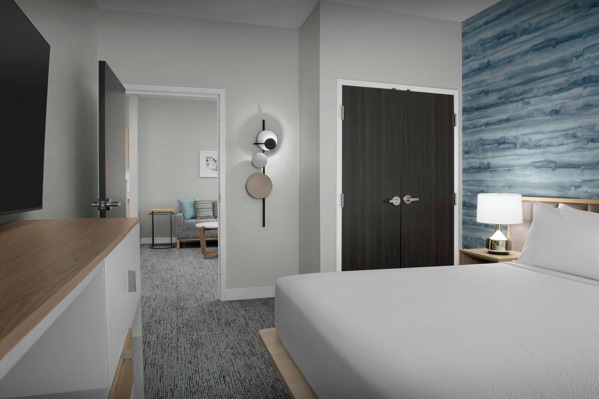 Hotelkamer met een bed, een bureau, een stoel, een kleine tafel, een lamp en een wand met een structuur.