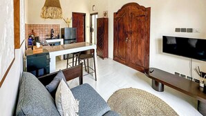 Ein großzügiger Wohnbereich mit Küche, einem großen Holzschrank, einem Flachbildfernseher und einer Sitzecke mit Sofa und Hocker.