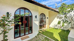 Ein modernes Haus mit großen Bogenfenstern, einem Ziegeldach und einem gepflegten Garten mit Rasenfläche und Kübelpflanzen.
