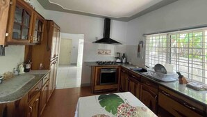 A kitchen with wooden cabinets, a stove, and a window with a view of greenery. - The Retreat (Lyssons)